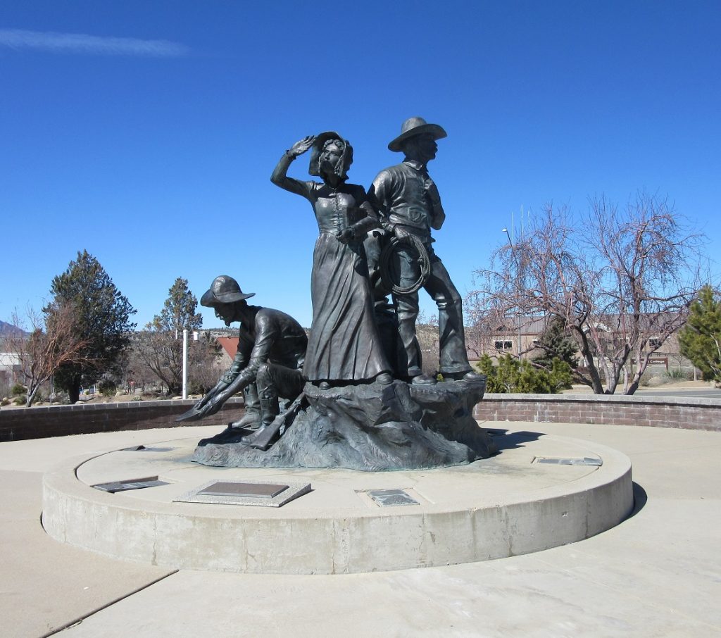 Statue of woman in long skirt, man in cowboy hat, and man squatting to pan for gold